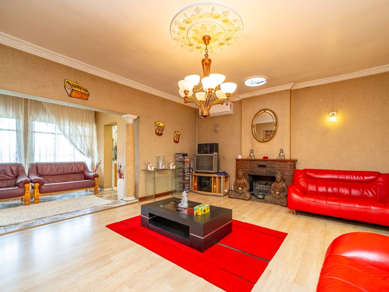 Spacious living room featuring a brick fireplace, decorative ceiling rose with chandelier, and an adjoining sunroom area with classic column detailing.