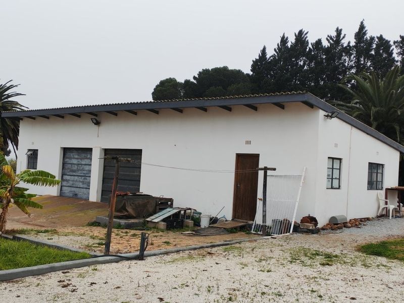Exterior view of a detached outbuilding or garage structure featuring a corrugated roof, exposed rafters, and double garage access doors.