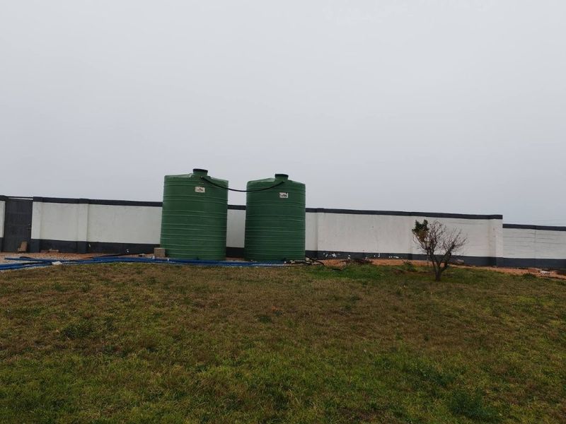 Outdoor area featuring two large green water storage tanks positioned against a perimeter boundary wall on the property grounds.