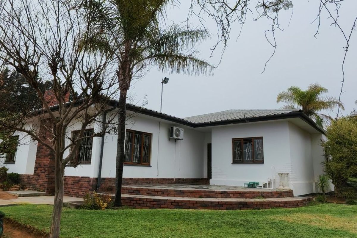 Rear view of the property featuring a brick patio, chimney, and established garden area with a metal roof and security bars on windows.