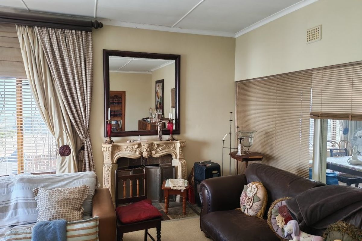 A living room featuring an ornate fireplace, neutral wall finishes, and window treatments including venetian blinds and curtains.