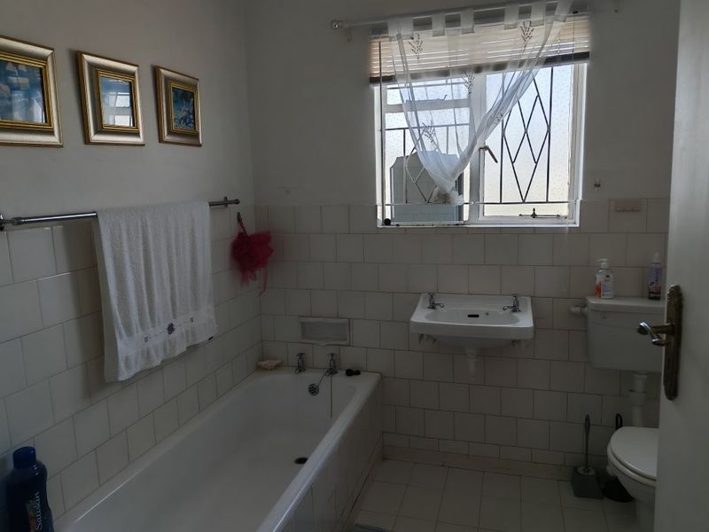 A functional bathroom featuring a bathtub, wall-mounted basin, and toilet, finished with ceramic wall tiling and a window with security bars.