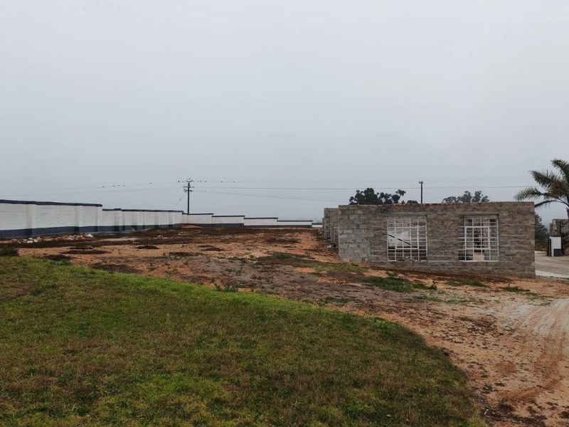 Rear view of the property showing an unfinished masonry structure, security bars on windows, and a long perimeter boundary wall on a large plot.