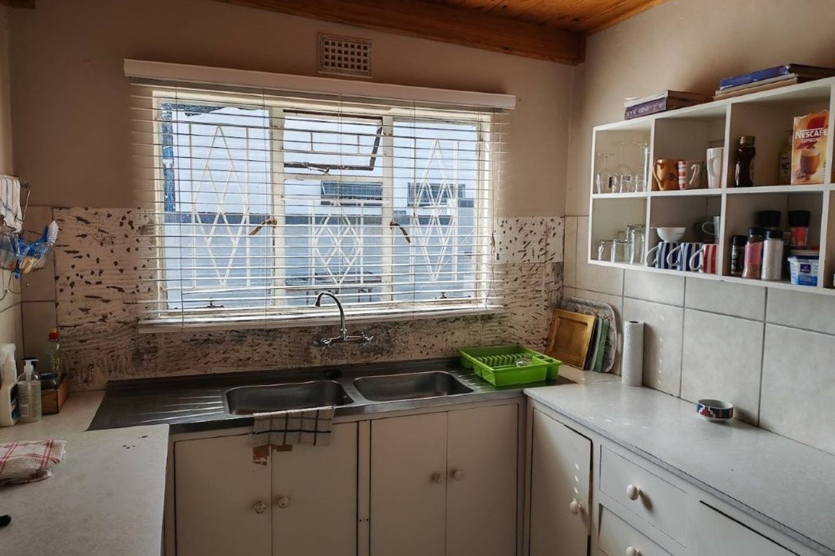 A functional kitchen featuring a double basin sink, laminate countertops, timber ceiling, and wall-mounted shelving, offering potential for modernization and aesthetic updates.