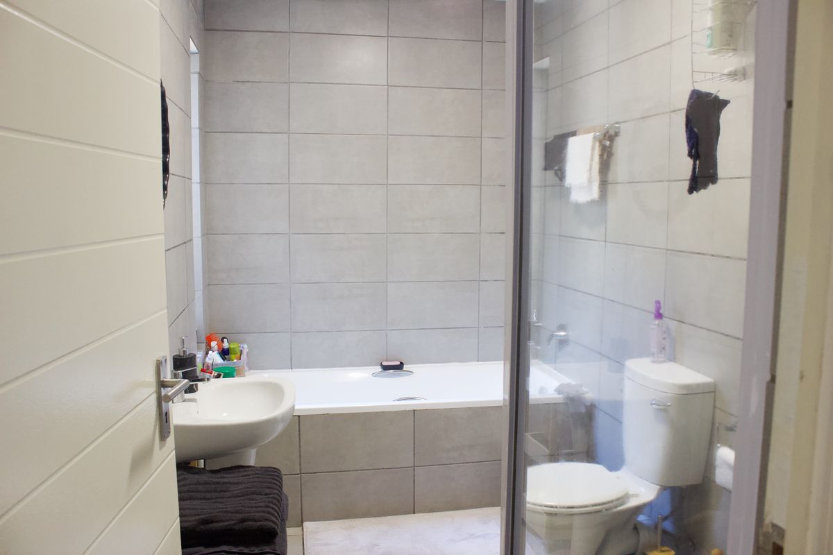 A modern bathroom featuring grey wall tiles, a bathtub, a wall-mounted basin, and a toilet with a glass shower screen.
