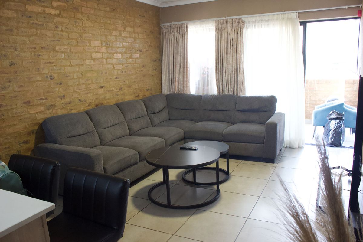 A living room featuring an exposed brick feature wall, neutral tiled flooring, and large sliding glass doors providing access to an outdoor area.