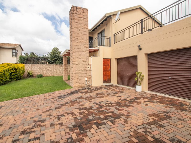 Front view of the property featuring a double garage, paved driveway, stone chimney, and an upper-level balcony with metal railings.