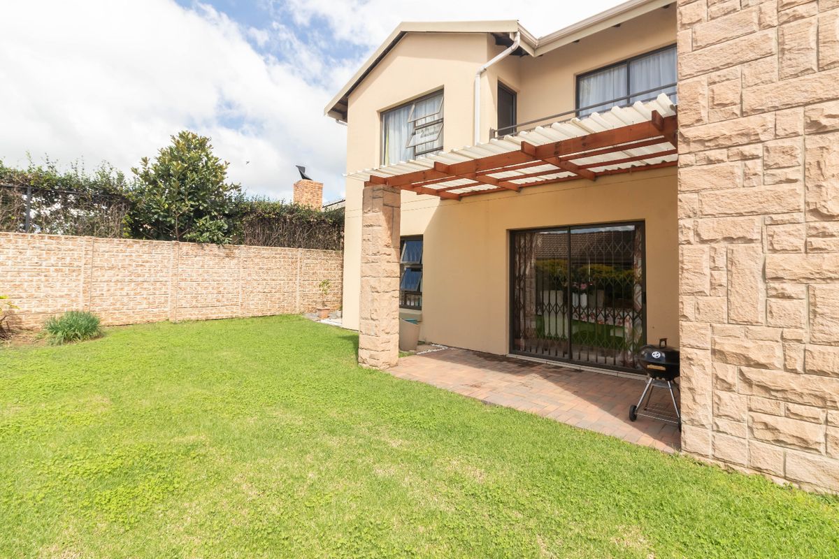 Rear view of the house featuring a paved patio with a pergola, stone-clad pillars, and a private garden with a boundary wall.