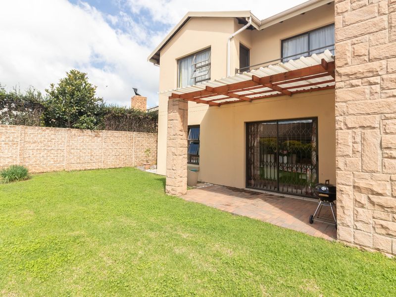 Rear view of the house featuring a paved patio with a pergola, stone-clad pillars, and a private garden with a boundary wall.