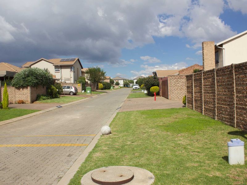 A view of a residential street within a housing estate, featuring paved roads, brick boundary walls, and landscaped verges.