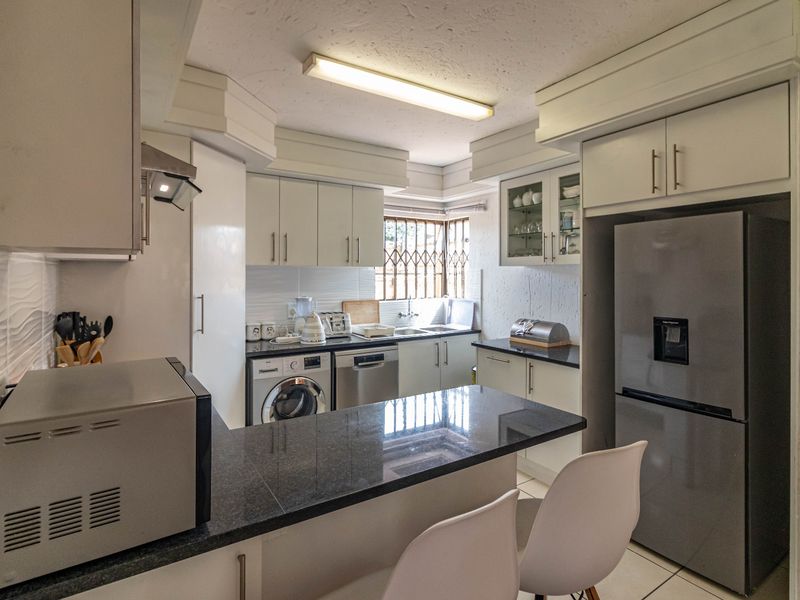 Functional kitchen featuring granite countertops, ample built-in cabinetry, and integrated laundry and dishwasher appliances, finished with a breakfast bar area.