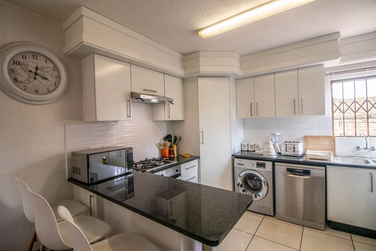 A functional kitchen featuring white cabinetry, granite countertops, a gas hob, and integrated space for laundry appliances.