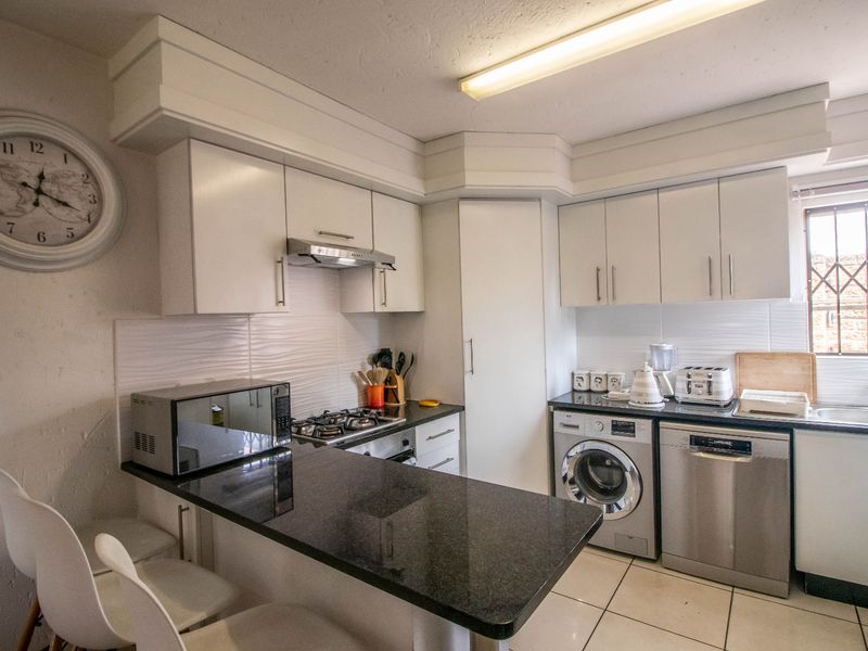 A functional kitchen featuring white cabinetry, granite countertops, a gas hob, and integrated space for laundry appliances.