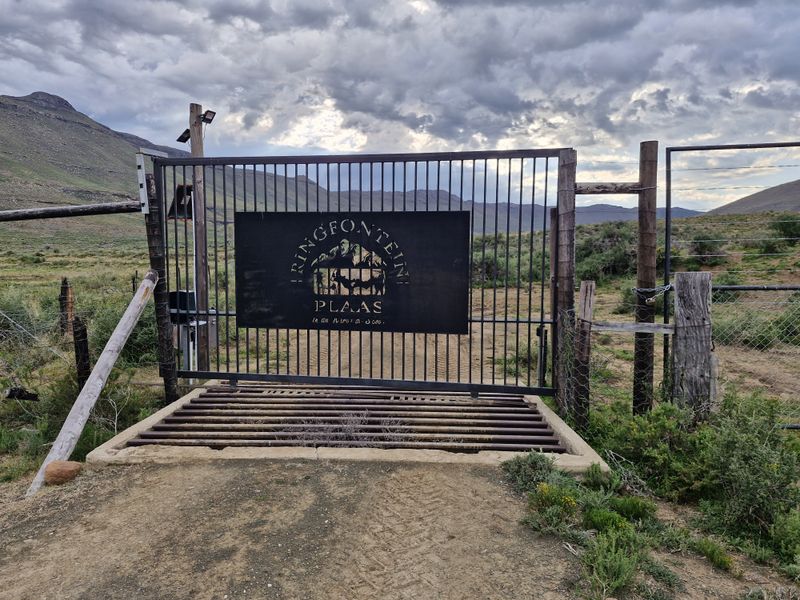 A secure metal farm gate entrance featuring a cattle grid and property signage, set against a rural landscape with mountain views.