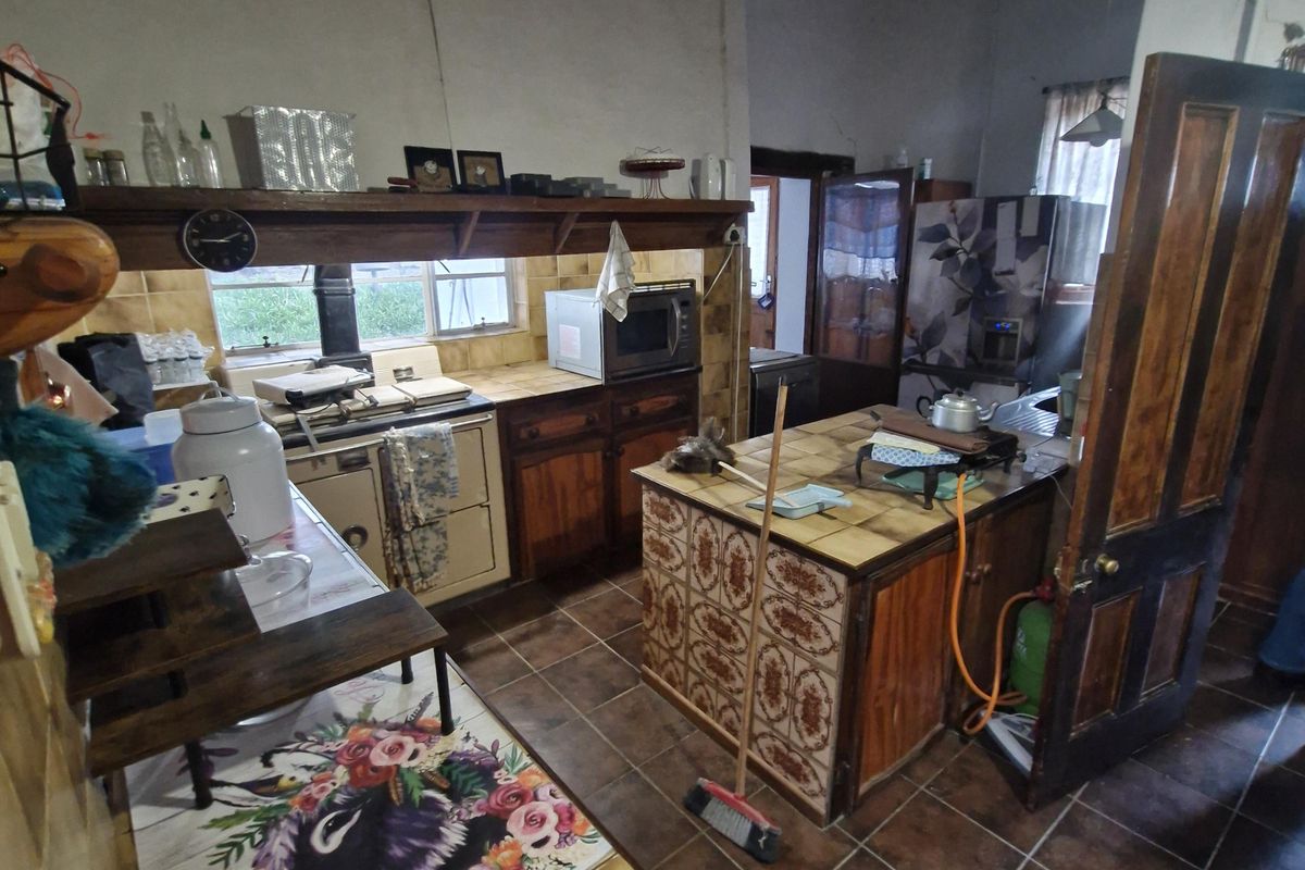 A rustic farm-style kitchen featuring tiled countertops, a central island, and exposed ceiling beams, offering a traditional layout with significant potential for modernization.