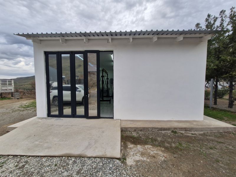 A detached utility building featuring a corrugated metal roof, exposed rafters, and modern black-framed bi-fold glass doors opening onto a concrete apron.