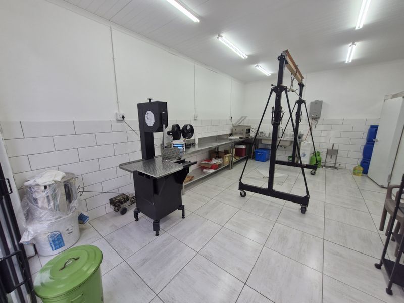 A clean, functional utility or processing space featuring tiled walls, durable tiled flooring, stainless steel prep surfaces, and industrial lighting.
