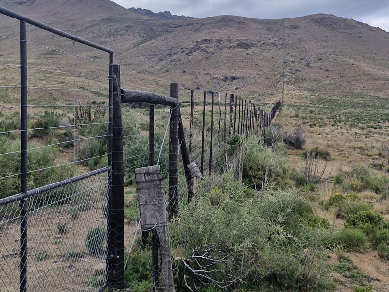 A view of the farm perimeter featuring wire mesh fencing and timber posts extending across the rugged landscape towards the mountains.