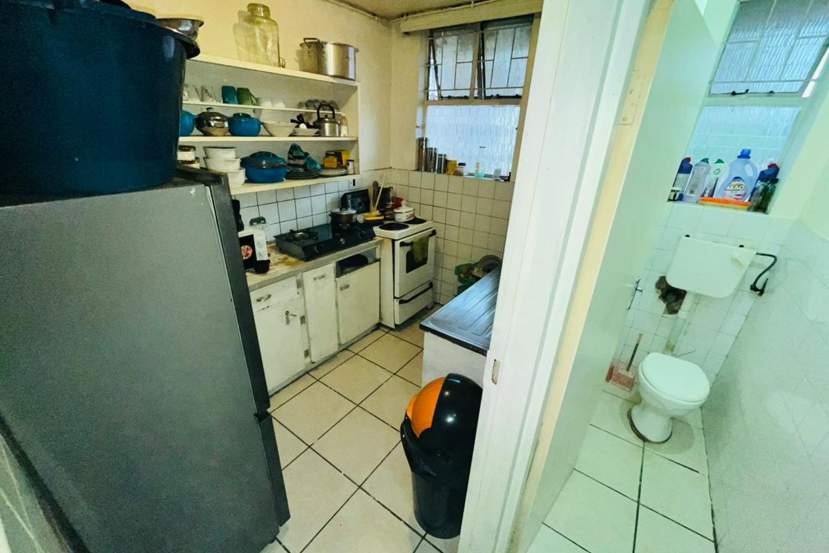 A compact kitchen area featuring tiled flooring, open shelving, and a freestanding stove, adjacent to a separate small bathroom facility.