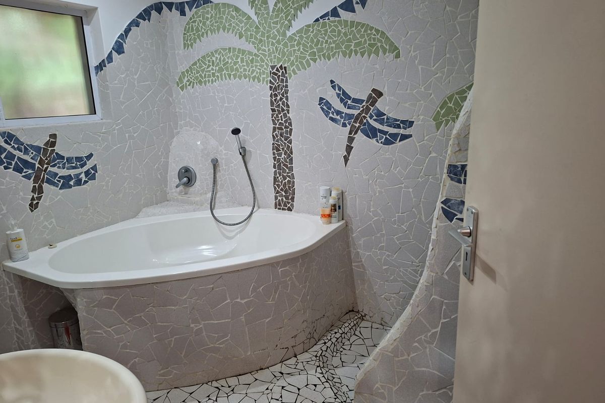 A bathroom featuring a corner bathtub with a custom mosaic tile surround and floor, showcasing a unique decorative palm tree and dragonfly design.