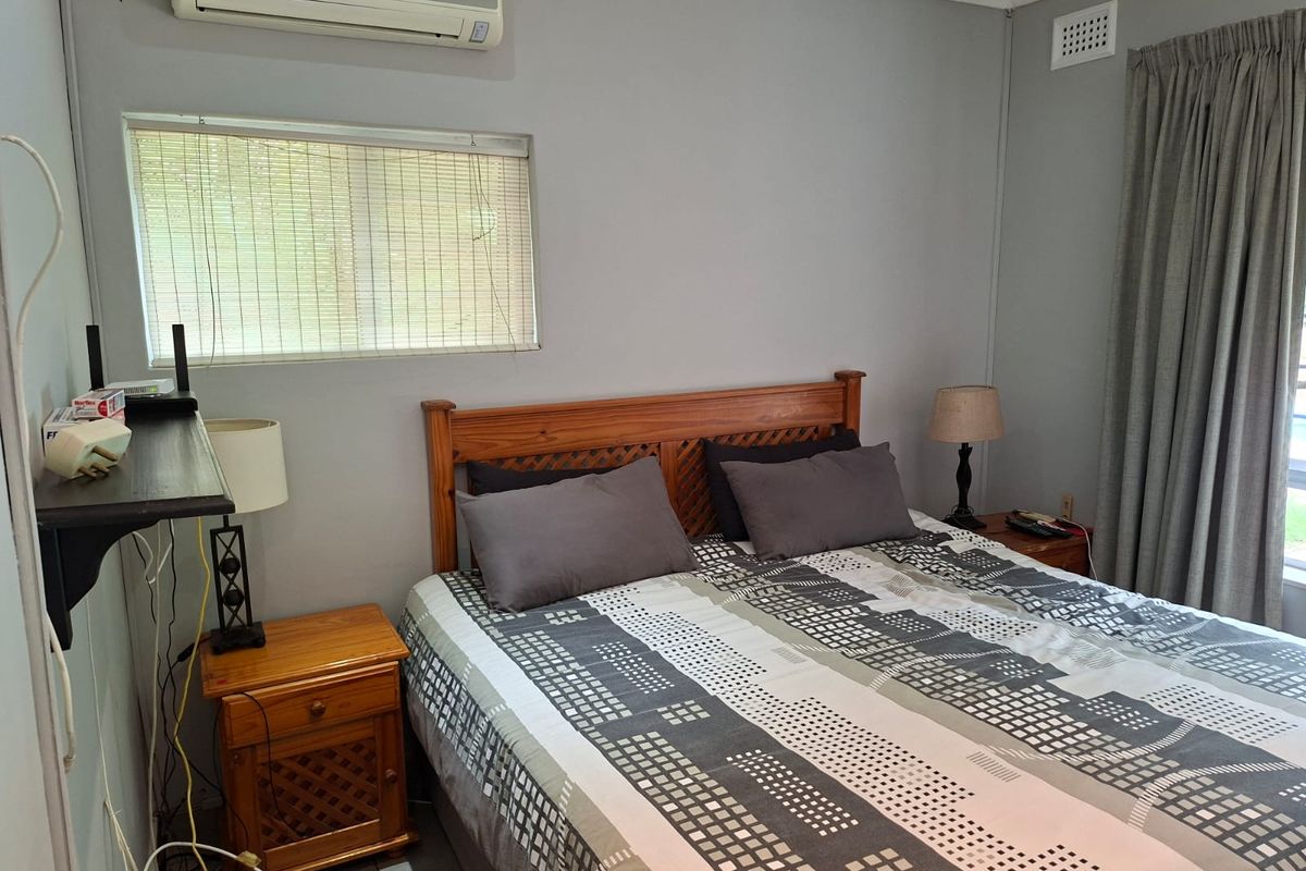 A functional bedroom featuring tiled flooring, a wall-mounted split-system air conditioner, and neutral wall finishes.