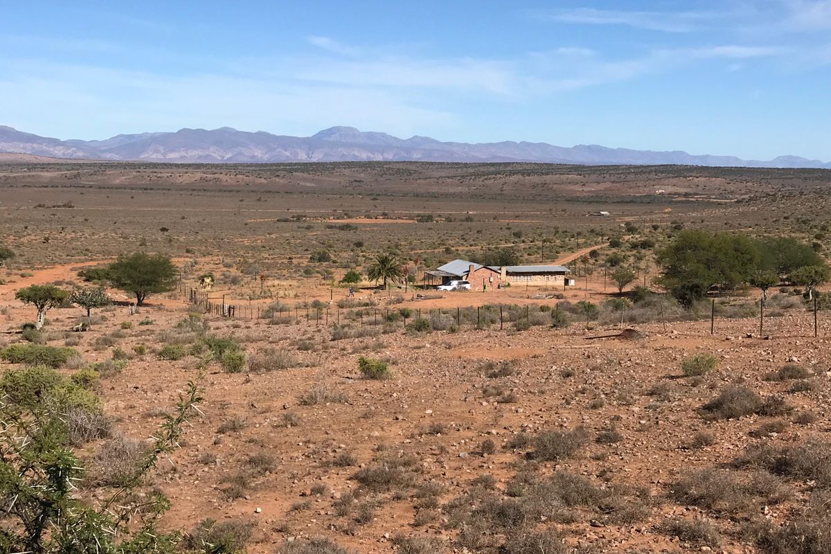 An elevated wide-angle view of a rural farm property set within a vast arid landscape with distant mountain ranges.