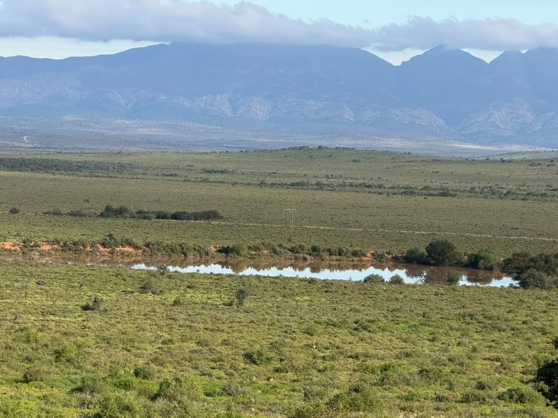 A scenic landscape view featuring a natural dam set against a backdrop of expansive rolling hills and a prominent mountain range.