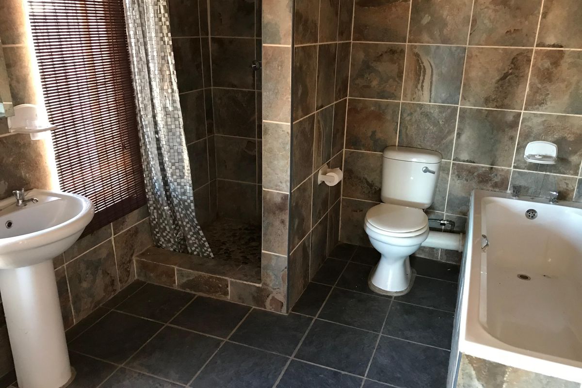 A functional bathroom featuring a pedestal basin, walk-in shower, toilet, and bathtub with natural stone-style wall tiling.