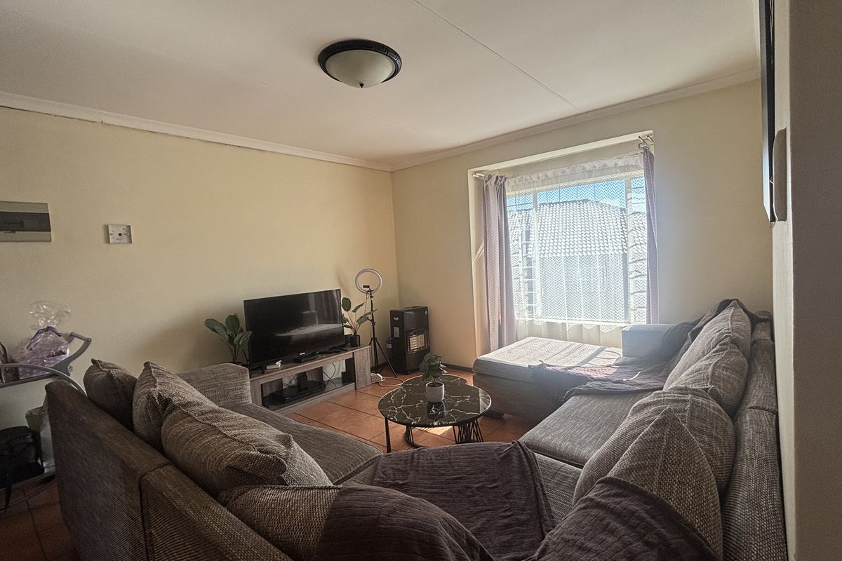 A comfortable living room featuring tiled flooring and a large window that allows for natural light, providing a functional space for relaxation.