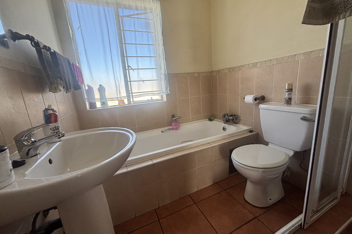 A functional bathroom featuring a pedestal basin, built-in bathtub, and toilet with neutral wall tiling and terracotta floor tiles.