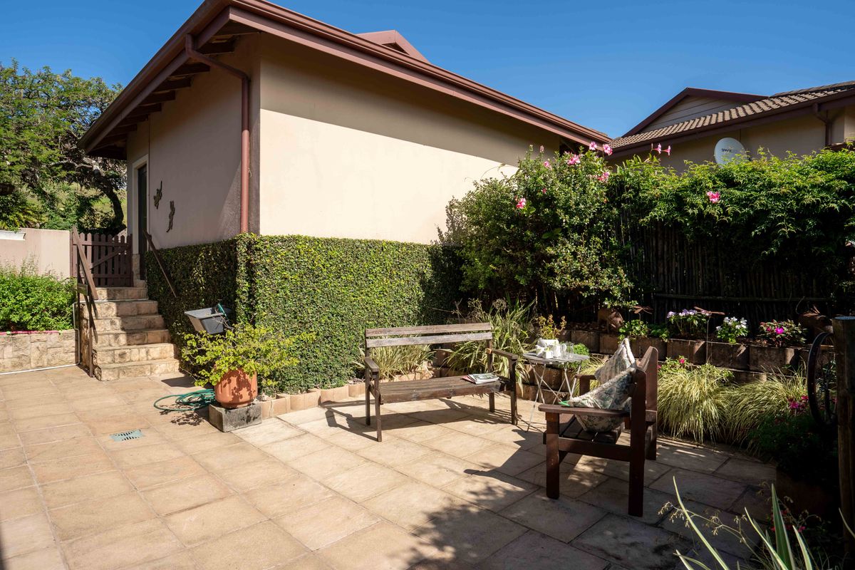 A private rear patio area featuring paved flooring, stone retaining walls, and an external staircase leading to the townhouse entrance.