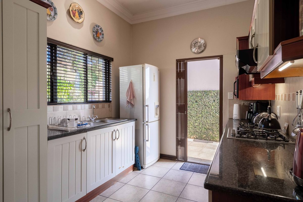 Functional kitchen featuring granite countertops, gas hob, double basin sink, and direct access to an outdoor area through a folding security door.