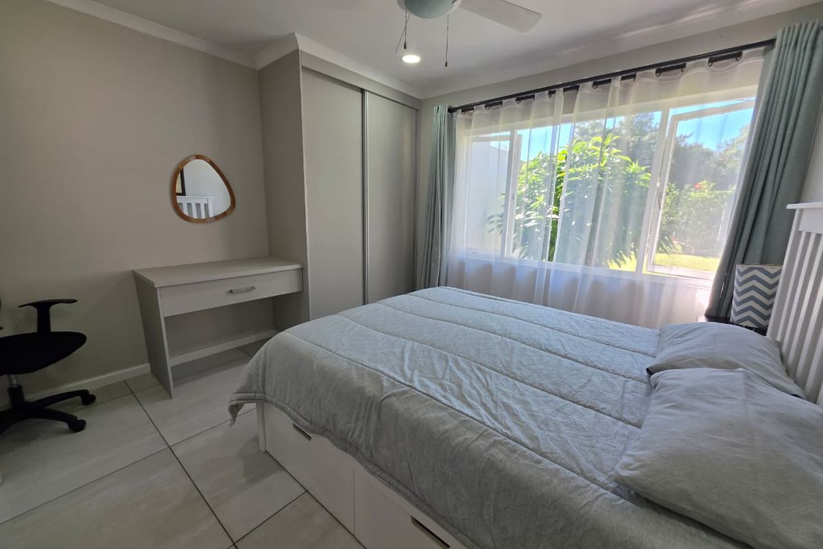 A well-maintained bedroom featuring neutral wall tones, tiled flooring, a built-in wardrobe, and a ceiling fan with natural light from the large window.