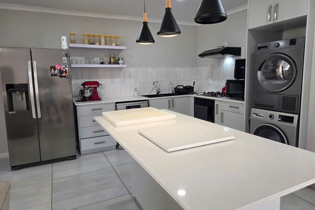 Modern kitchen featuring a central island with quartz countertops, built-in appliances, sleek cabinetry, and tiled flooring, offering a functional and contemporary cooking space.