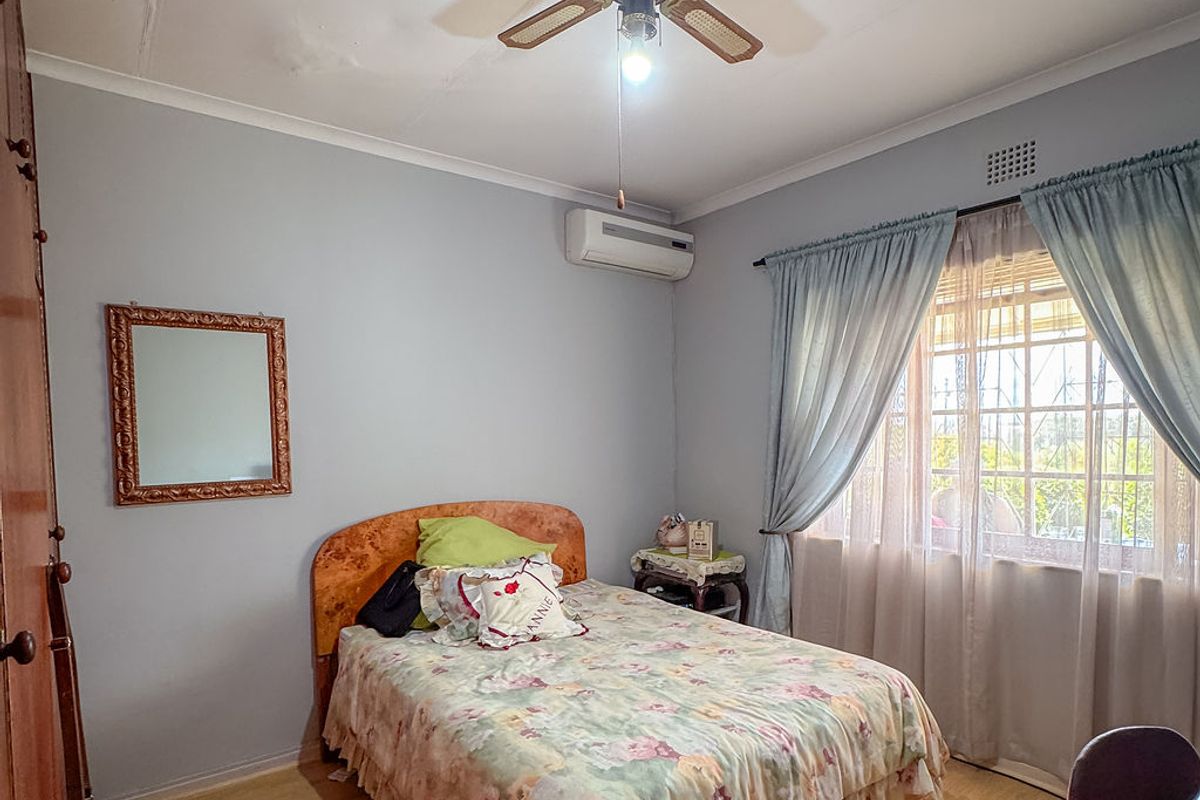 A functional bedroom featuring laminate flooring, a ceiling fan, and a wall-mounted air conditioning unit, with visible signs of ceiling water damage.