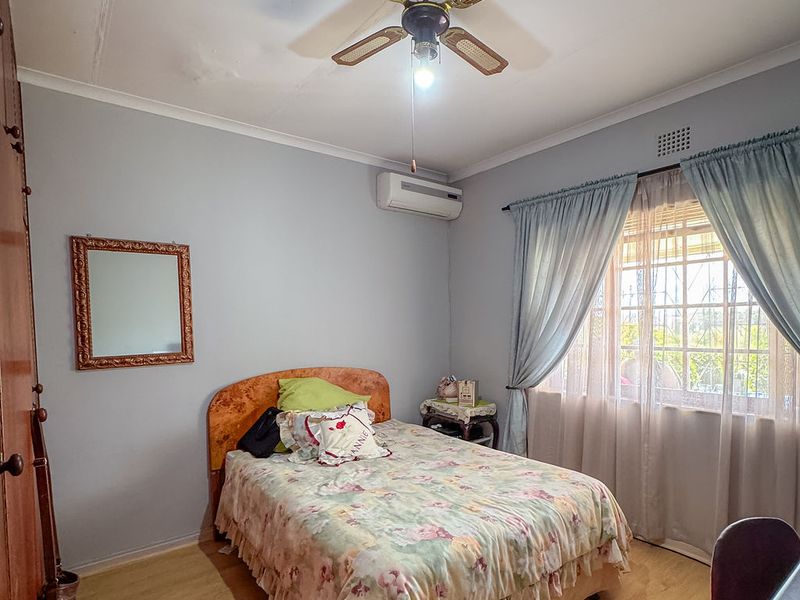 A functional bedroom featuring laminate flooring, a ceiling fan, and a wall-mounted air conditioning unit, with visible signs of ceiling water damage.