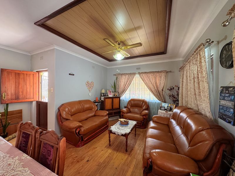 A cozy living room featuring warm timber flooring, a distinctive timber-paneled ceiling with a central fan, and a classic stable-style door.