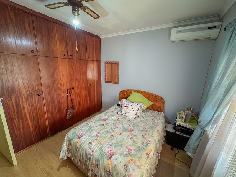A functional bedroom featuring extensive built-in wooden cabinetry, a ceiling fan, and a wall-mounted air conditioning unit with laminate flooring throughout.
