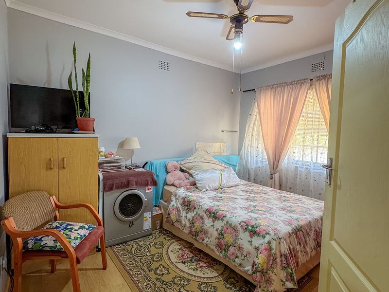 A bedroom featuring laminate flooring, a ceiling fan, and a window with curtains, providing a functional living space.