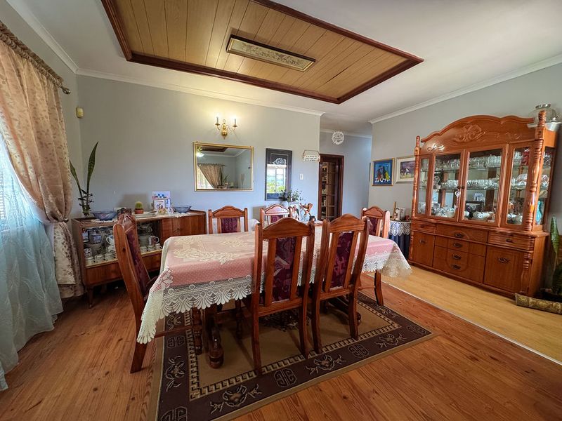 A traditional dining room featuring timber flooring, a decorative recessed ceiling panel, and wall-mounted lighting fixtures.