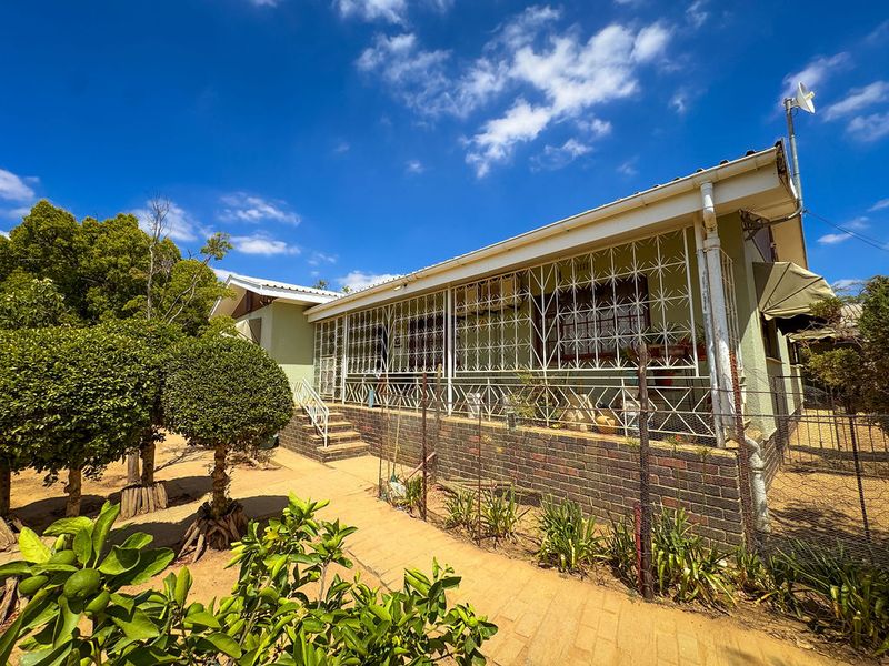 Rear view of the house featuring a covered patio, brick foundation, and security bars, set within a garden area with a paved walkway.