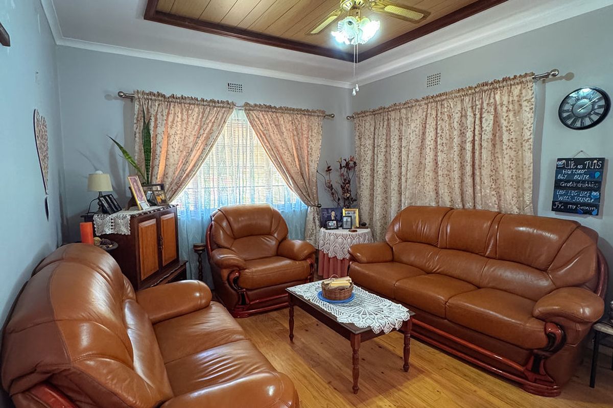 A living room featuring polished hardwood flooring, a timber-paneled ceiling with a central ceiling fan, and classic cornice detailing.