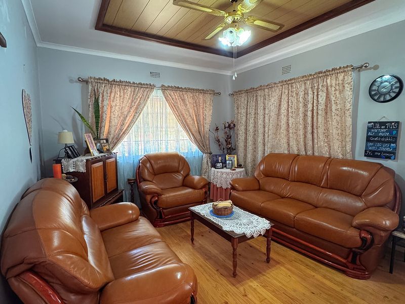 A living room featuring polished hardwood flooring, a timber-paneled ceiling with a central ceiling fan, and classic cornice detailing.