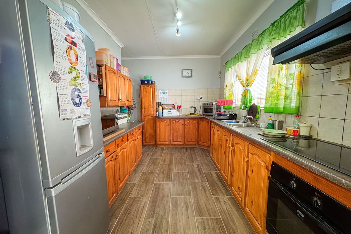 A functional kitchen featuring wooden cabinetry, laminate countertops, built-in oven, electric hob, and tiled flooring, offering a practical layout for daily meal preparation.