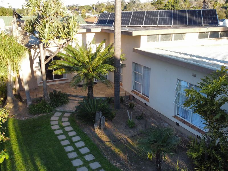 Aerial view of the rear exterior featuring a paved patio area, established garden, and roof-mounted solar panels on a corrugated metal roof.