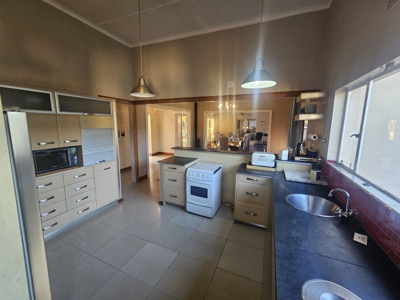 A functional kitchen featuring light wood cabinetry, a freestanding stove, dark countertops, and a tiled splashback, with an open-plan flow to the dining area.