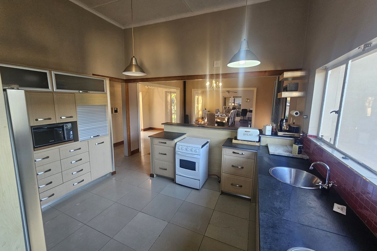 A functional kitchen featuring light wood cabinetry, a freestanding stove, dark countertops, and a tiled splashback, with an open-plan flow to the dining area.