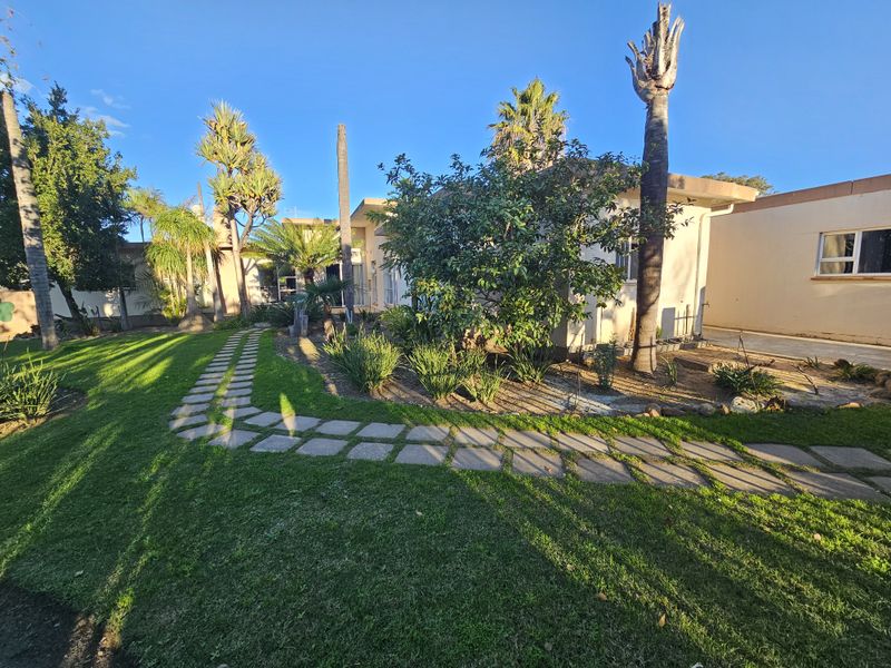 A well-maintained rear garden featuring a paved walkway, established trees, and direct access to the home via sliding glass doors.