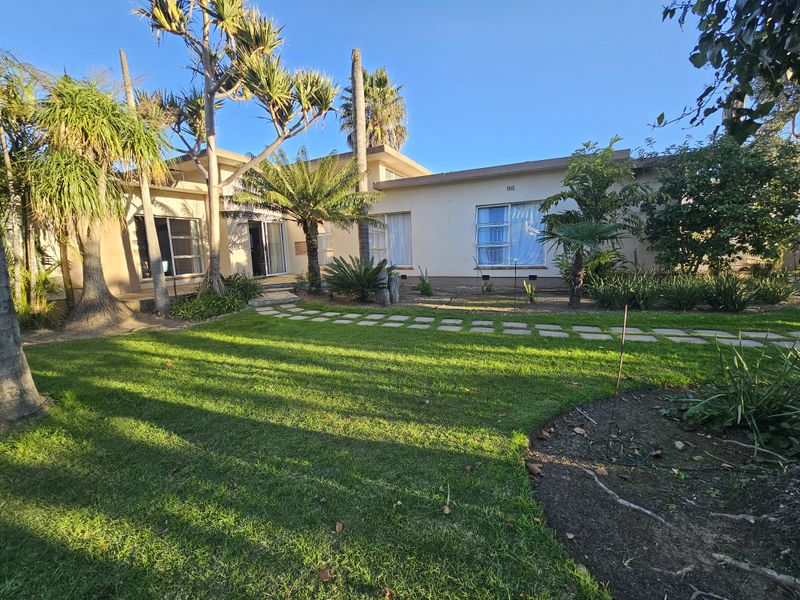 A view of the rear elevation of the house featuring a well-maintained lawn, landscaped garden, and paved pathway leading to the sliding glass doors.