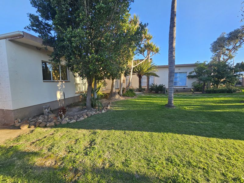 A spacious rear garden featuring a well-maintained lawn, mature trees, and stone landscaping, providing a private outdoor area for the property.